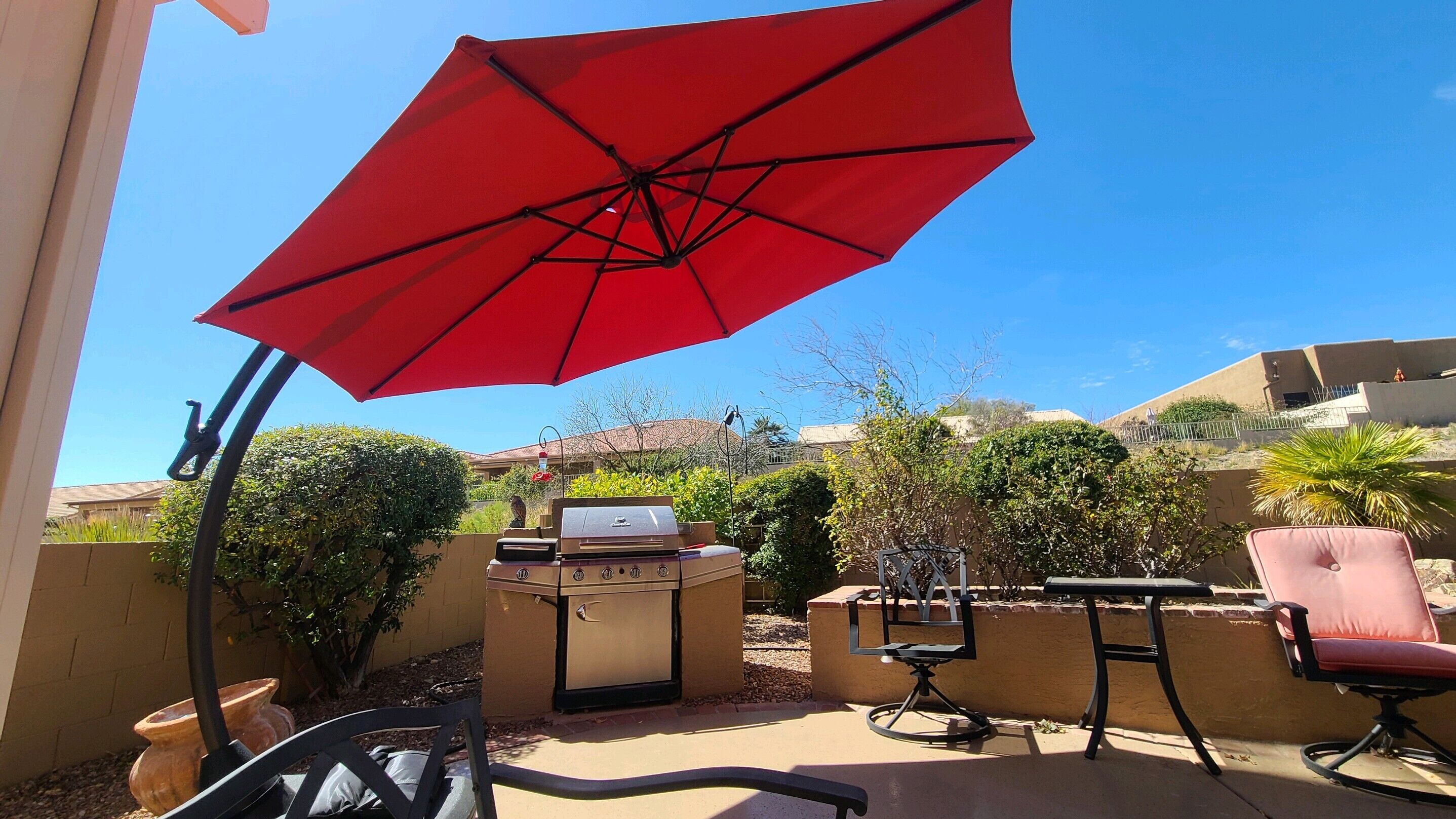 A patio area with a red umbrella, a grill, and outdoor furniture.