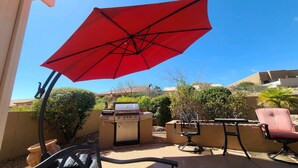 Un patio con sombrilla roja, una parrilla y mobiliario exterior.