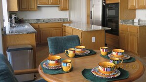 Una cocina moderna con armarios de madera, un refrigerador de acero inoxidable y una mesa de comedor con tazas y platillos coloridos.