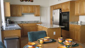 A modern kitchen with wooden cabinets, a stainless steel refrigerator, and a dining table set with colorful cups and saucers. - Mountain Views from Front and Back Patios (Tucson)