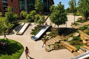 A playground with slides and steps, surrounded by trees and a building in the background. - The Cary Cottage 1 BR 1 BA Private Sleeps 4 - Downtown Cary, Eat Drink Play Shop (Cary)
