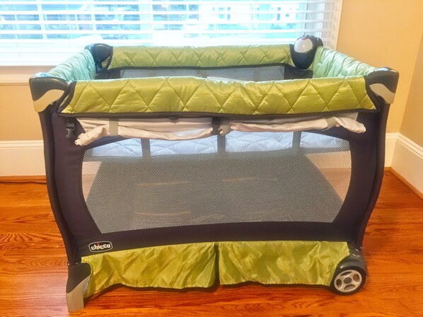 A portable playpen with a green and black color scheme, placed on a wooden floor near a window. - The Cary Cottage 1 BR 1 BA Private Sleeps 4 - Downtown Cary, Eat Drink Play Shop (Cary)