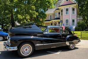 A classic black convertible car parked on a street with a large house in the background.