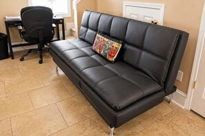 A black leather sofa with a colorful cushion, a black office chair, and a tiled floor. - The Cary Cottage 1 BR 1 BA Private Sleeps 4 - Downtown Cary, Eat Drink Play Shop (Cary)