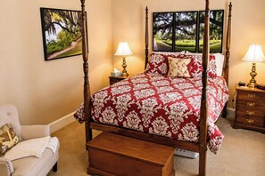 A four-poster bed with a red and white damask bedspread, two bedside lamps, a nightstand with a lamp, and a chair with a blanket.