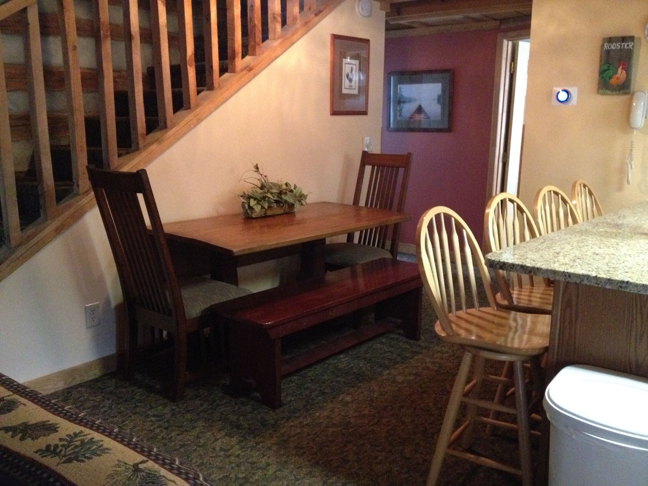 A dining area with a wooden table, chairs, a bench, and a staircase.