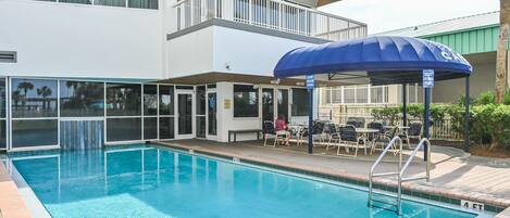 A pool area with a blue umbrella, outdoor seating, and a two-story building with balconies.