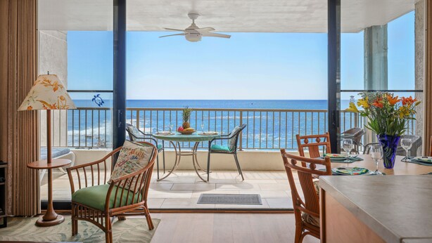 Ein Balkon mit Tisch und Stühlen, einem Deckenventilator und Blick auf den Ozean.