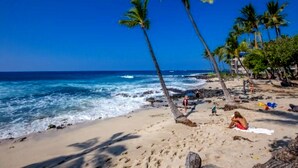 Ein Strand mit Palmen, Meereswellen und entspannenden Menschen.
