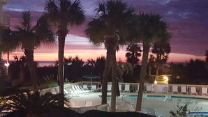 A pool area with lounge chairs and palm trees, surrounded by a fence. - Beachfront/Oceanfront Hilton Head Island Condo (Hilton Head)