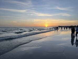 Een strand met een zonsondergang, golven en mensen die langs de kust wandelen.