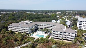 A modern hotel with a curved architecture, multiple balconies, and a central swimming pool surrounded by palm trees. - Beachfront/Oceanfront Hilton Head Island Condo (Hilton Head)