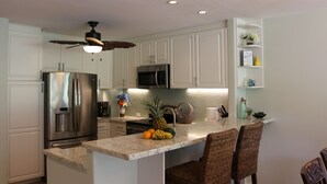 A modern kitchen with white cabinets, a stainless steel refrigerator, a microwave, and a ceiling fan. -  A/C, Deluxe, Top Floor, Quiet Development, heated pool, convenient location (Princeville)