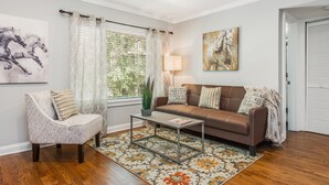 Una sala de estar con un sofá de cuero marrón, un sillón estampado, una mesa de centro y un tapete floral.