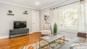 Una sala de estar con televisor, sofá, mesa de centro y plantas decorativas.