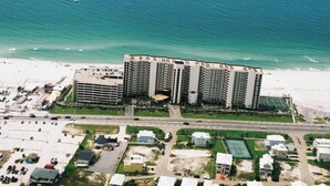 A high-rise hotel with multiple floors, a parking lot, and a beach in the background. - Phoenix10 Beach front condo fully upgraded with brand new custom bathrooms. (Orange Beach)