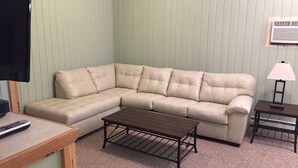 A beige sectional sofa, a wooden coffee table, a small table with a lamp, and a remote control on a wooden side table. - Cozy and comfortable 1,000 sq. ft. 2-bedroom home with garage. (Bellaire)