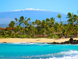 A beach with palm trees, ocean waves, and a mountain in the background. - 3 Bedroom Spacious Waikoloa Beach Resort (Waikoloa Village)