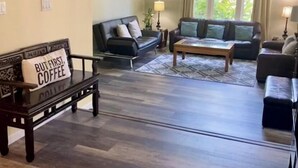 A spacious living room with a wooden floor, two sofas, a coffee table, and a wall sign that reads "Welcome to our home".