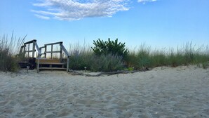 En strand med en trækonstruktion, muligvis en redningsstation, omgivet af sand og sparsom vegetation.