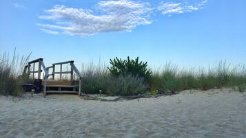 Una playa con una estructura de madera, posiblemente un puesto de salvavidas, rodeada de arena y vegetación escasa.