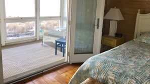 Et soveværelse med en seng, et natbord, en lampe, en stol og en dør, der fører ud til en balkon.
