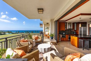 A balcony with wicker furniture, a kitchen area, and a view of the ocean.