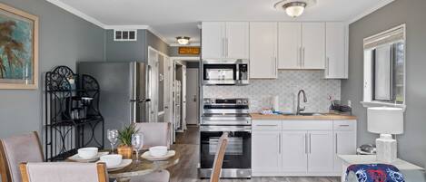 A modern kitchen with white cabinets, stainless steel appliances, and a dining area with a round table and chairs.
