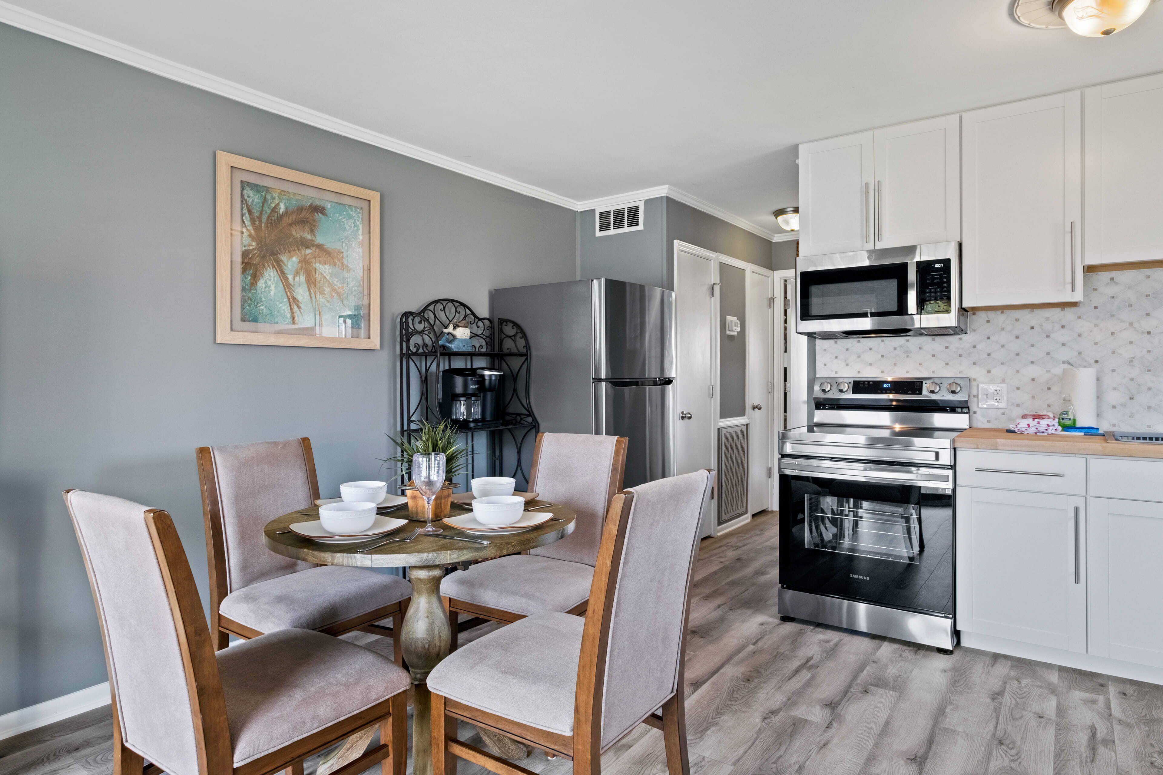 A modern kitchen with white cabinets, stainless steel appliances, and a dining area with a round table and cushioned chairs.