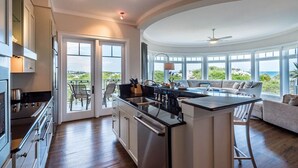 A modern kitchen with a central island, large windows, and a view of the ocean.