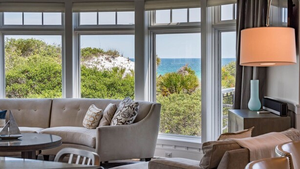 A room with a sofa, armchairs, and a table, large windows with a view of the sea and greenery.