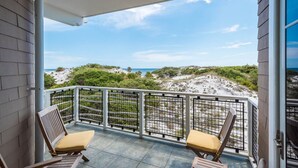 A balcony with two wooden chairs and a view of the beach.