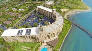 An aerial view of a resort with a large pool, a marina, and a curved building with multiple floors. - Serene Ocean-Front Condo at Menehune Shores - Unit 520 - Steps from the Ocean! (Kihei)