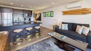 Une cuisine moderne avec un îlot central, des tabourets de bar, un canapé et une table basse dans l’espace salon.
