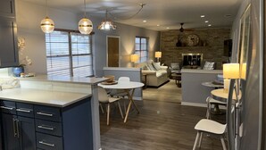 A modern kitchen with a central island, dining area with chairs, a living room with a sofa and coffee table, and a brick accent wall. - 3/2
1 Mile to Main St! (Fredericksburg)