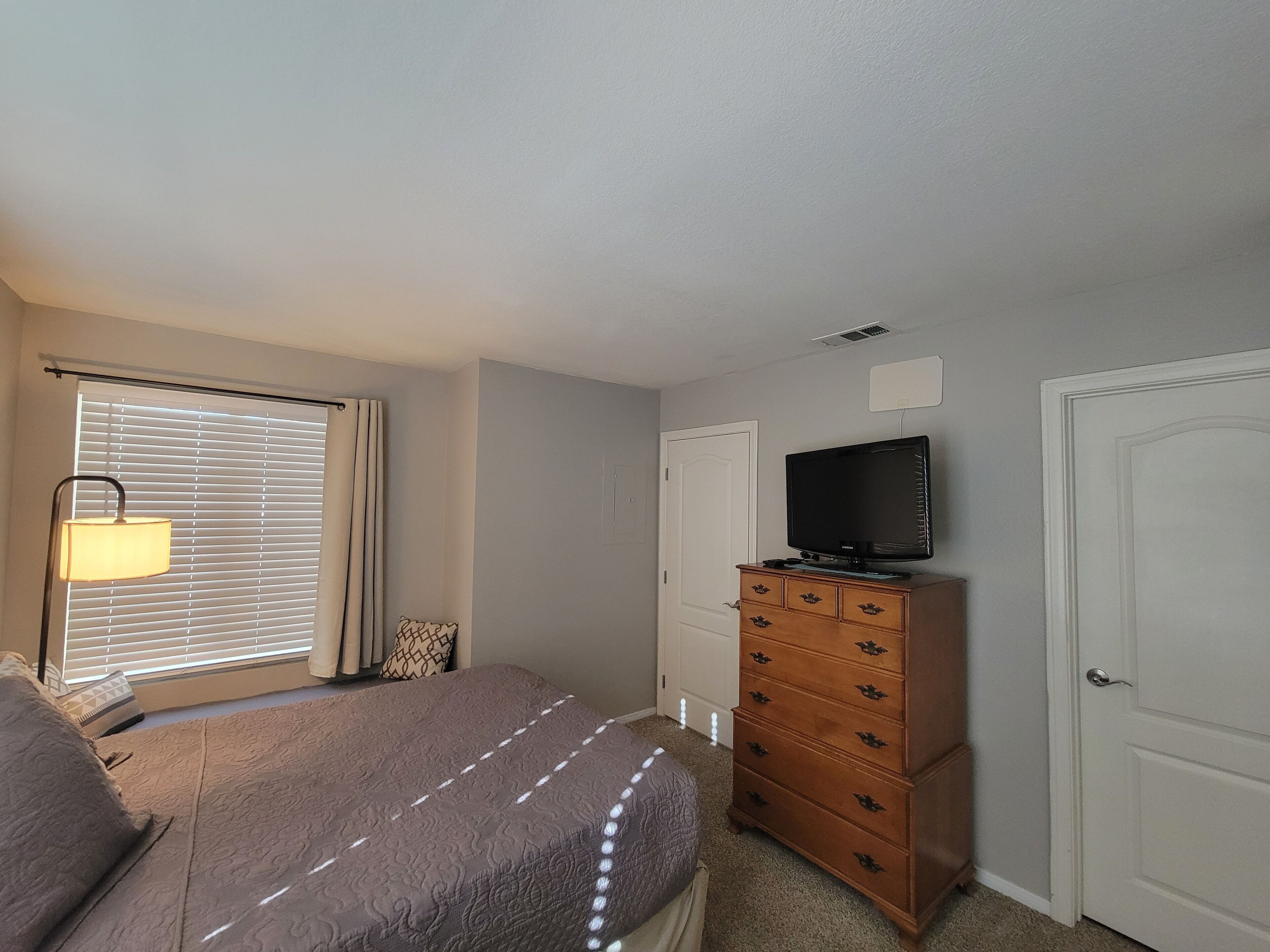 Een slaapkamer met een bed, dressoir, televisie en een raam met zonwering.