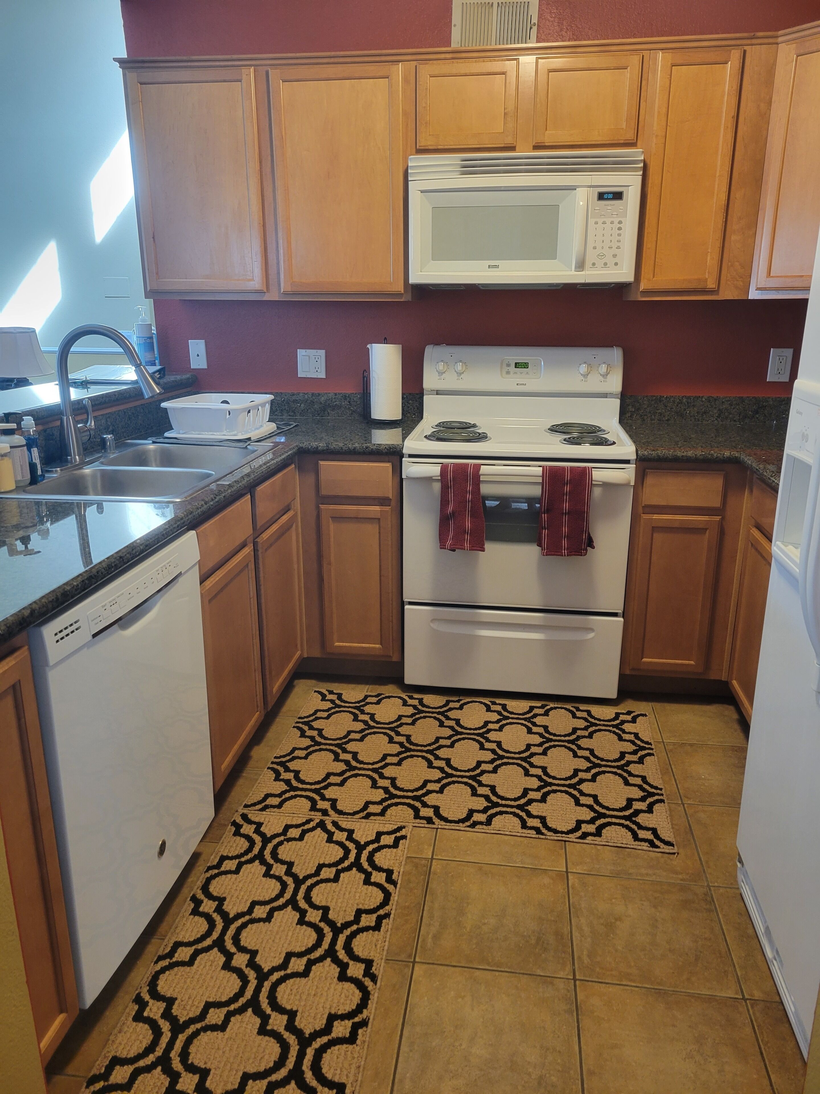A kitchen with wooden cabinets, a white stove, a microwave, and a patterned rug.