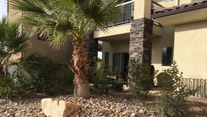 A residential building with a stone and stucco exterior, a palm tree, and a landscaped garden with rocks and grass.