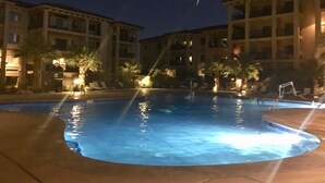 A nighttime swimming pool with surrounding buildings and palm trees.