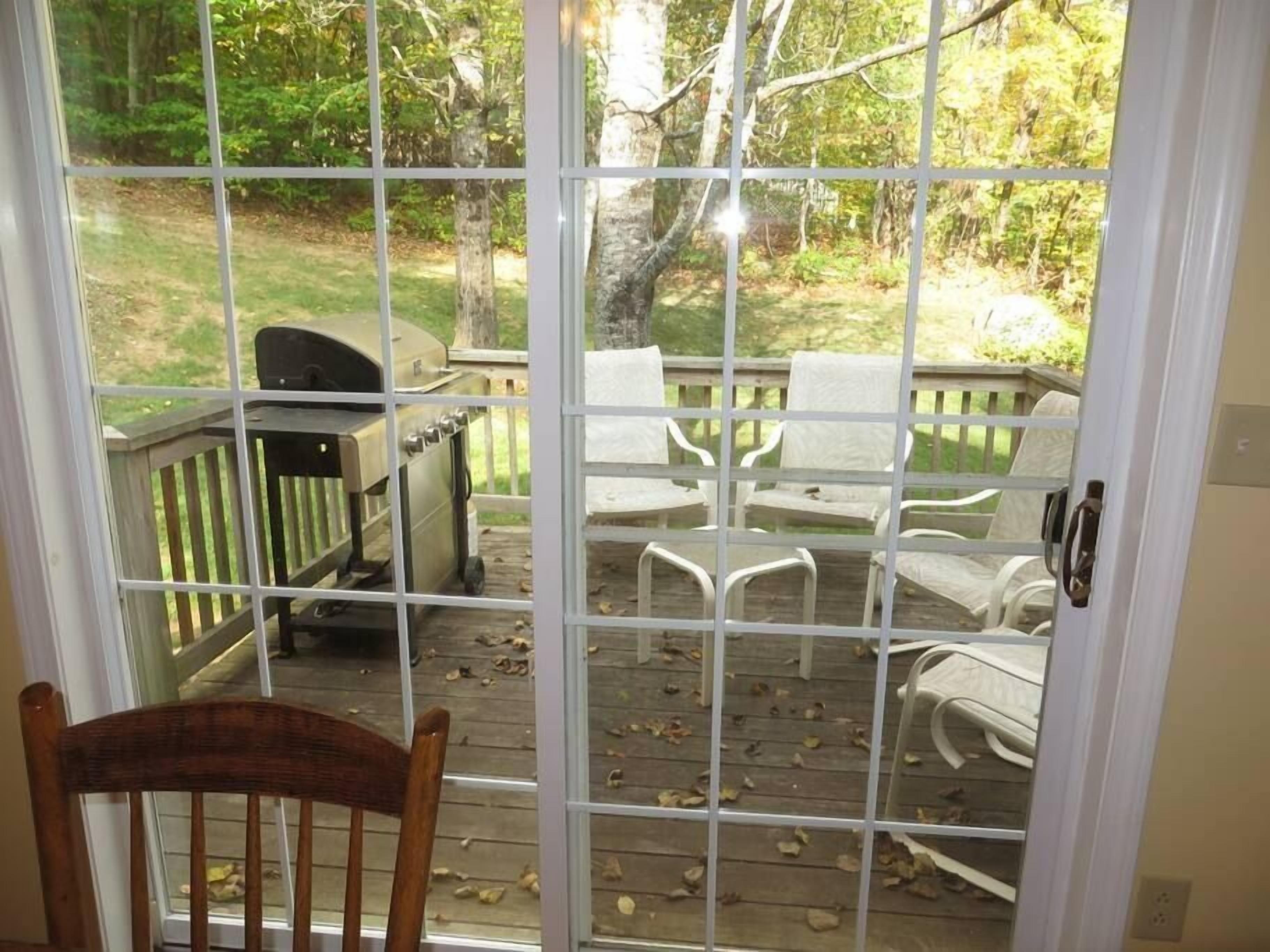 Uitzicht door een raam op een terras met buitenmeubels en een barbecue.