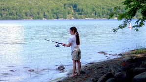 A person fishing by a lake with a boat visible in the background. - The Lily Pad at Loon Lake near Gore Mountain (Chestertown)