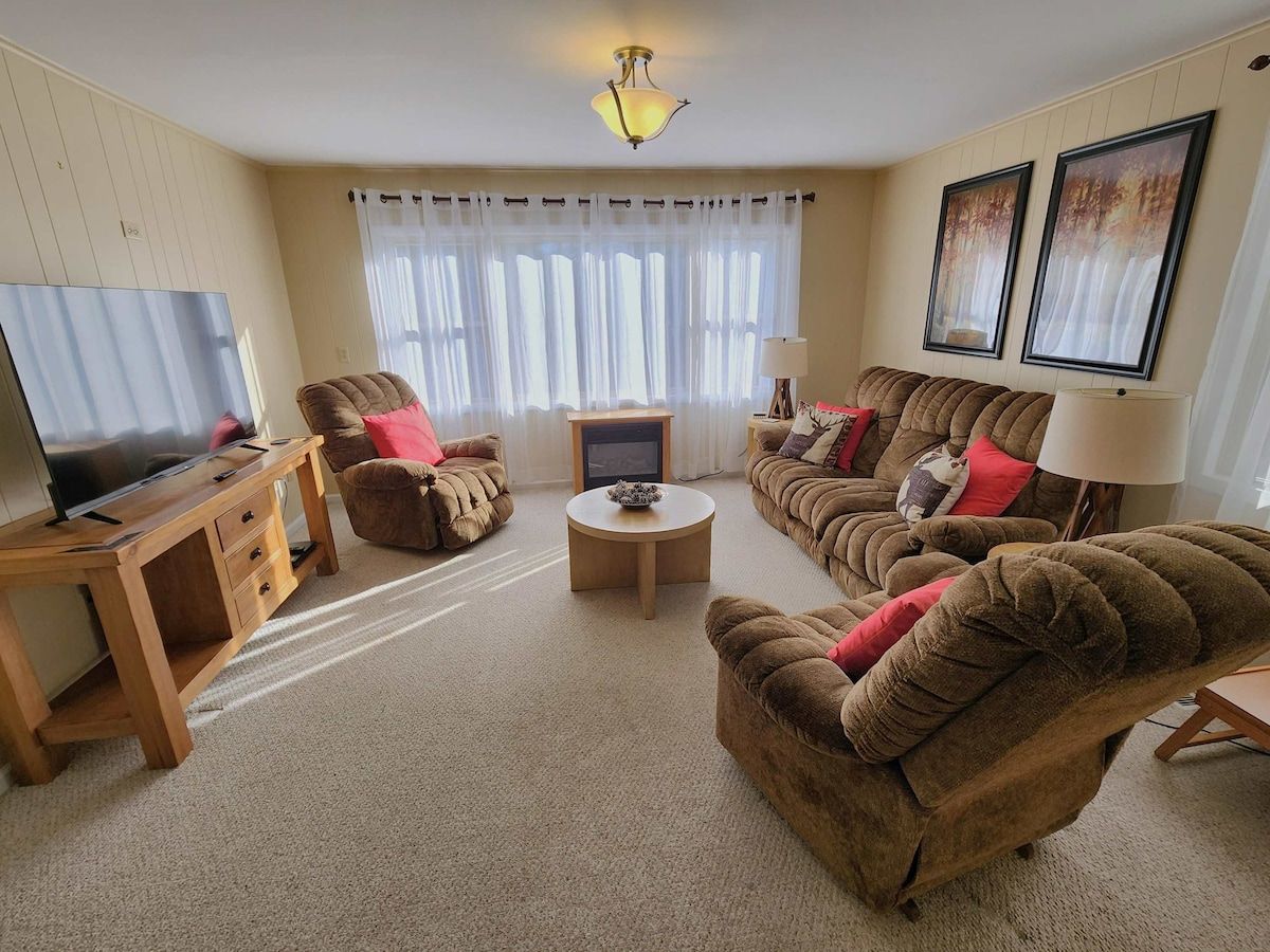 Een woonkamer met een televisie, bank, fauteuil, salontafel en een open haard.