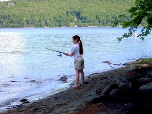 Une personne est en train de pêcher au bord d’un lac, avec un bateau visible au loin.