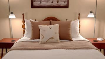 A bedroom with a large bed, two bedside lamps, a framed picture on the wall, and a nightstand with a lamp.