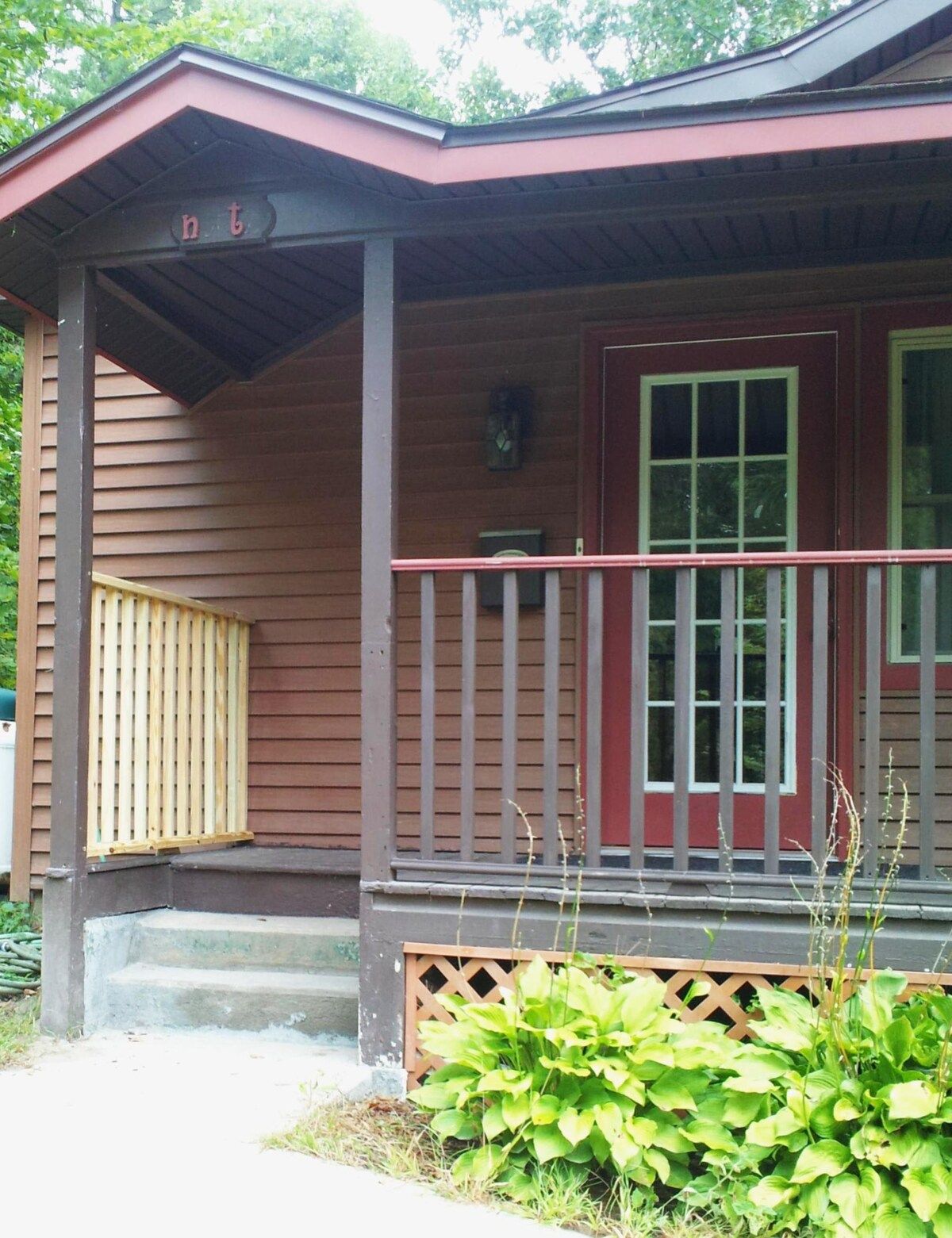 Un bâtiment en bois doté d’un porche, d’une porte rouge et d’une petite fenêtre.