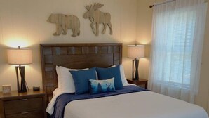 A bedroom with a large bed, two bedside tables with lamps, and wall art of a bear and moose. - The Lily Pad at Loon Lake near Gore Mountain (Chestertown)