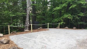 Sorapäällysteinen pysäköintialue, jossa on köysiaita ja kiviä, ja jonka ympärillä on metsäinen alue.