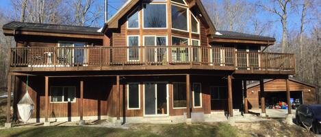 A two-story wooden cabin with a balcony, large windows, and a garage.