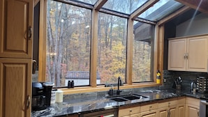 Eine moderne Küche mit Holzausstattung, einer schwarzen Arbeitsplatte und einem großen Fenster mit Blick auf einen Wald.