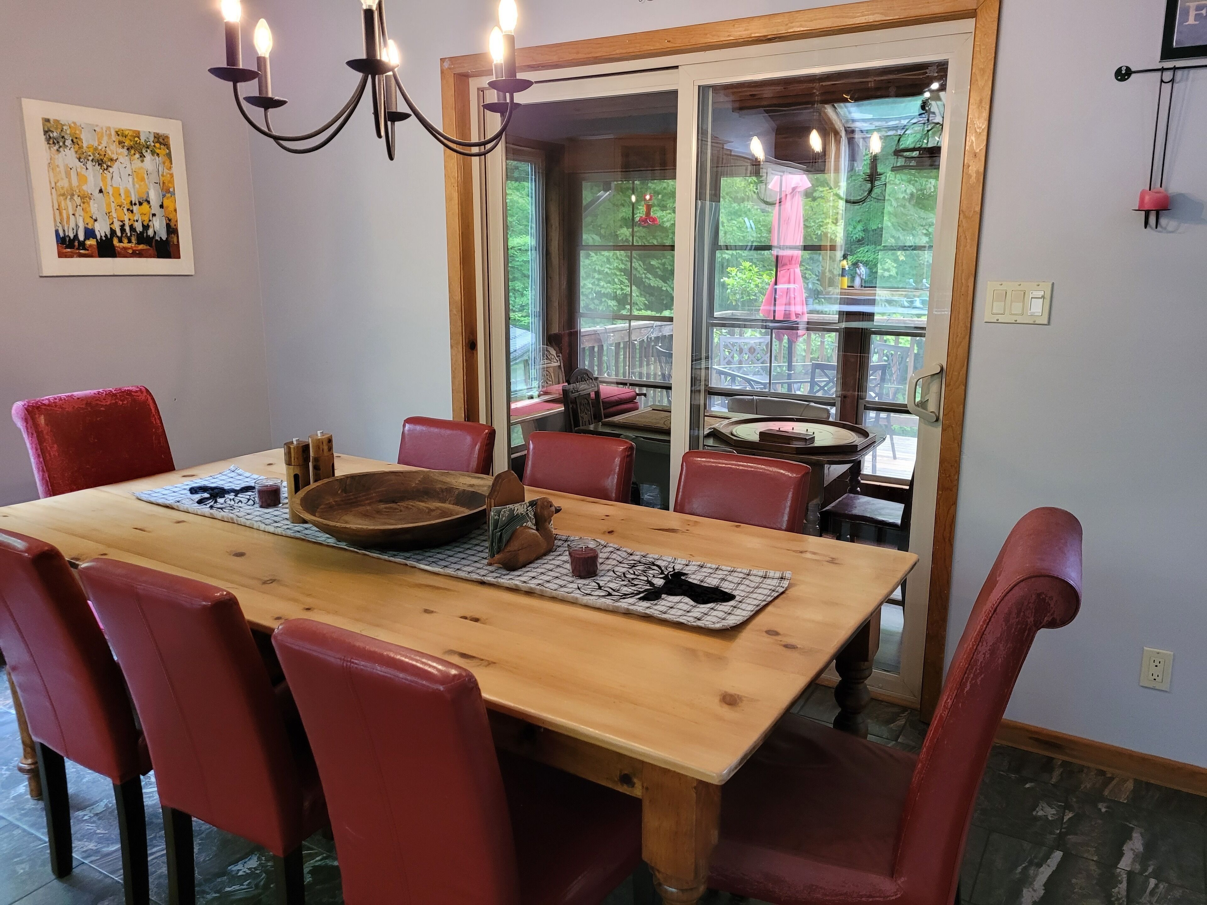 A dining area with a wooden table, red chairs, a chandelier, and a glass door leading outside.